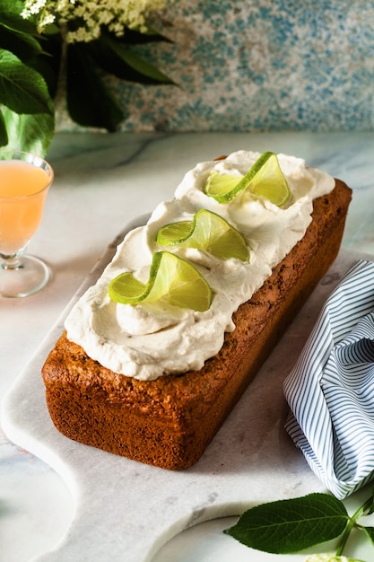 Sommer süßer Laib Kuchen auf einem Tisch mit Blumen und einem Getränk in Gläsern. mit Kokoscreme und Limette. Dessert zum Brunch oder Frühstück am Morgen