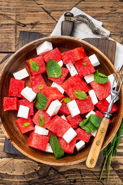 Sommer-Wassermelonensalat mit Feta-Käse und Minze in einer Holzplatte. Hölzerner Hintergrund. Ansicht von oben.