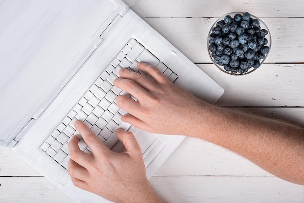 Sommerblaubeeren auf einem weißen Holztisch mit einem kreativ bemalten Laptop