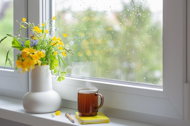 Sommerblumen im weißen Krug mit einer Tasse Tee auf der Fensterbank