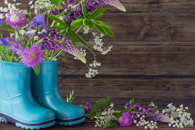 Sommerblumen in Gummistiefeln auf altem dunklem Holz