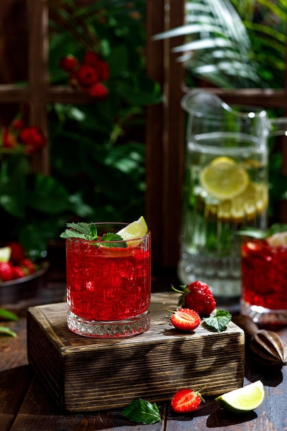 Sommercocktail mit roten Erdbeeren in einem Glas auf dem Tisch neben dem Fenster. In den Strahlen der Sonne