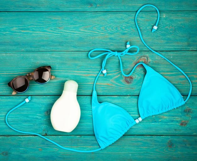 Sommerdamenmode mit blauer Badeanzug-Sonnenbrille und Sonnencreme auf blauem Holzschreibtisch