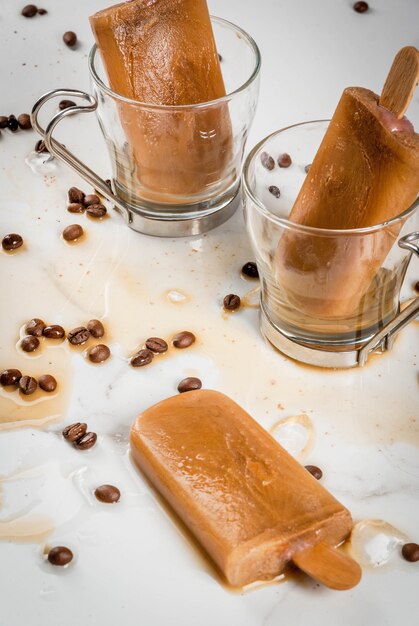 Sommerdesserts. Gefrorene Getränke. Süßes Eis am Stiel aus Kaffee und Milch. In Kaffeetassen Auf einem weißen Marmortisch mit Kaffeebohnen.