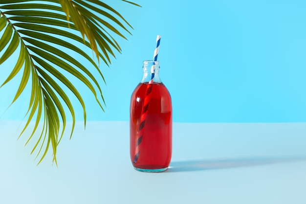 Sommereis-Cranberry-Punsch-Cocktail in Flasche mit Palmblatt auf blauem Hintergrund