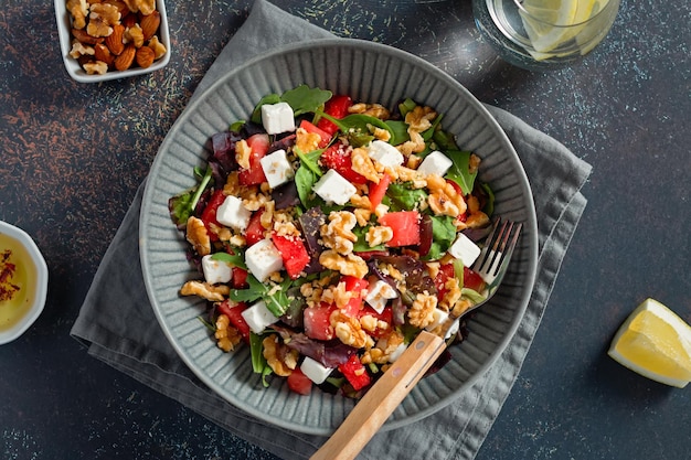 Sommererfrischender Salat mit Wassermelonen-Feta-Käse, Walnüssen und Gemüse auf schwarzer Tischplatte mit Zitronenwasser-Draufsicht Rezept für Hitzewelle