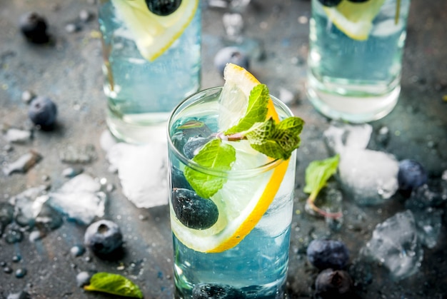 Sommererfrischungsgetränke, Blaubeerlimonade oder Mojito-Cocktail mit Zitrone, frischen Blaubeeren und Minze, sdark blauer Stein copyspace