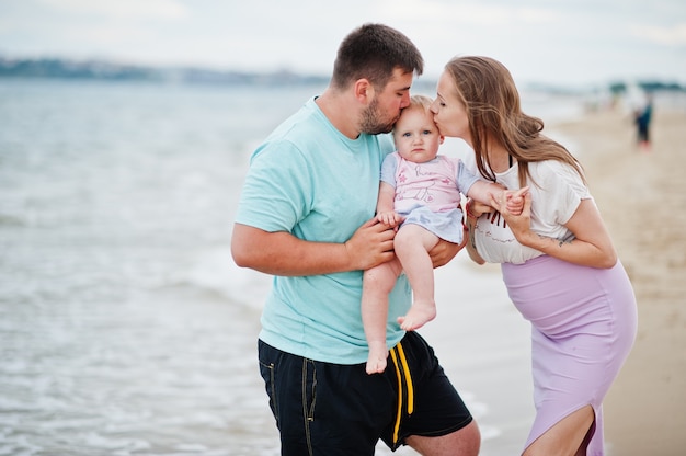 Sommerferien. Eltern und Menschen im Freien mit Kindern. Schöne Familienferien. Vater, schwangere Mutter, Tochter am Meersandstrand.