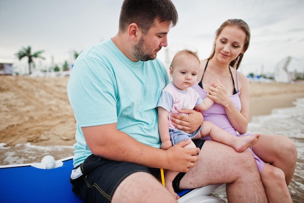 Sommerferien Eltern und Menschen Outdoor-Aktivitäten mit Kindern Fröhliche Familienferien Vater schwangere Mutter Baby Tochter sitzt auf Sonnenliege am Meeressandstrand