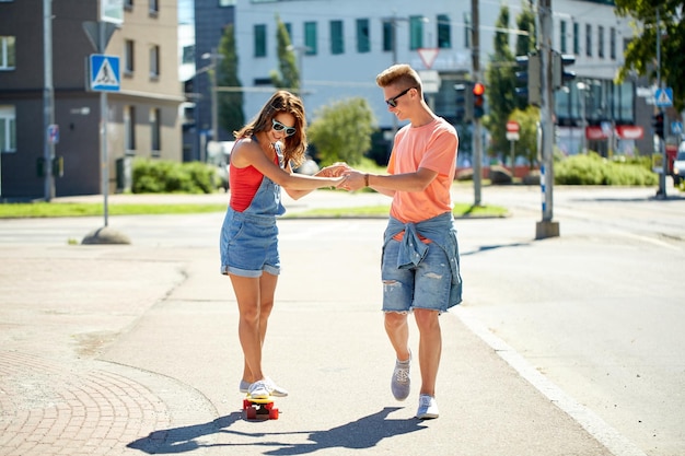 Sommerferien, Extremsport und Menschenkonzept - glückliches Teenager-Paar reitet kurzes, modernes Cruiser-Skateboard auf der Stadtstraße