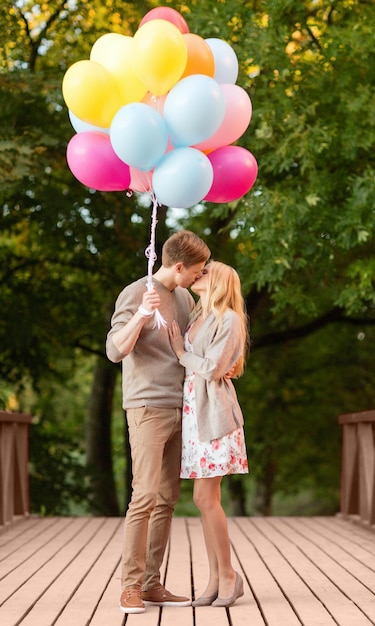Sommerferien, Feiern und Dating-Konzept - Paare mit bunten Luftballons, die sich im Park küssen