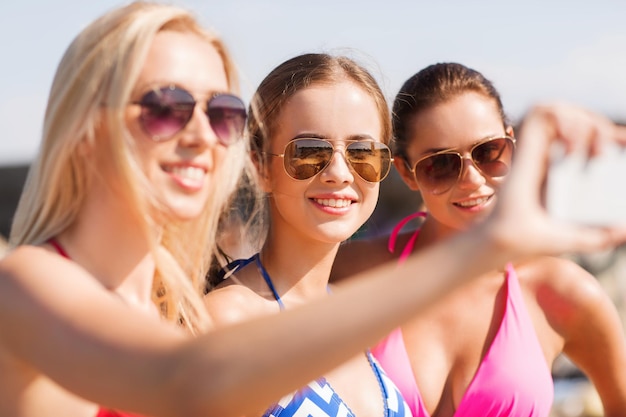 sommerferien, ferien, reisen, technologie und personenkonzept - gruppe lächelnder junger frauen am strand, die selfie mit smartphone über blauem himmelhintergrund machen