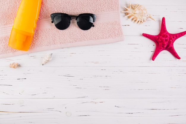 Sommerferien-Ferienkonzept. Sonnencreme und Sonnenbrille auf einem Handtuch um Muscheln und Sea Star. Draufsicht und Flachlage