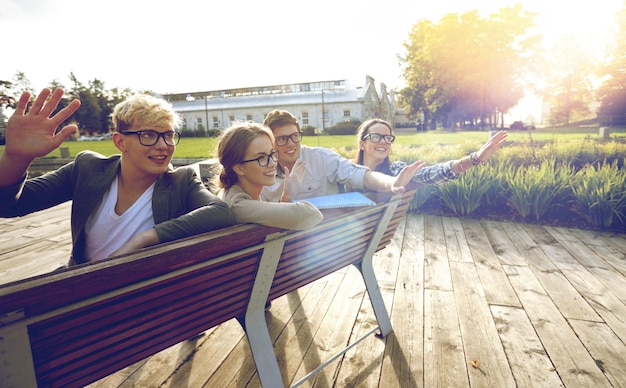 Foto sommerferien, freundschaft, freizeit- und teenagerkonzept - gruppe von studenten oder jugendlichen, die auf dem campus oder im park herumhängen und hände winken