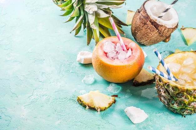 Sommerferien-Getränkkonzept, stellen verschiedene tropische Cocktails oder Säfte in der Ananas, in der Pampelmuse und in der Kokosnuss mit Eis, hellblauer Beton ein