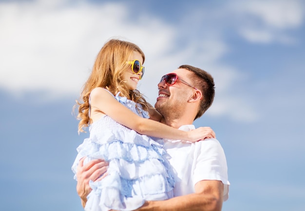 Sommerferien, Kinder- und Menschenkonzept - glücklicher Vater und Kind mit Sonnenbrille über blauem Himmel