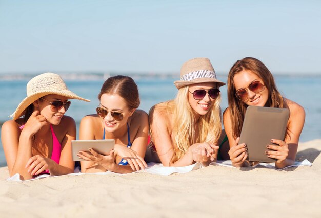 sommerferien, reisen, technologie und personenkonzept - gruppe lächelnder frauen mit sonnenbrillen und tablet-pc-computern, die am strand liegen