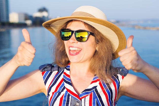 Sommerferien und Ferien - junge Frau zeigt Daumen hoch am Strand.