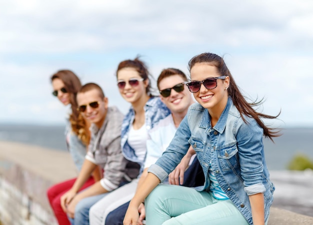 sommerferien und teenagerkonzept - lächelndes teenagermädchen mit sonnenbrille, das draußen mit freunden rumhängt