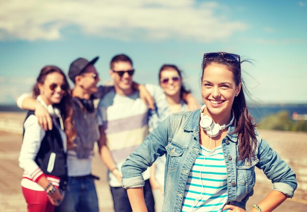 sommerferien und teenagerkonzept - teenagermädchen mit sonnenbrille und kopfhörern, die draußen mit freunden abhängen