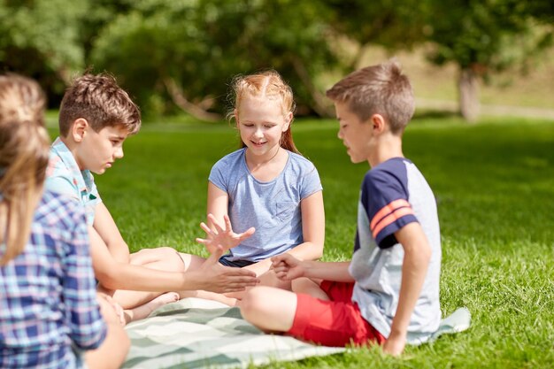 sommerferien, unterhaltung, kindheit, freizeit und menschenkonzept - gruppe glücklicher vorteener kinder, die im park ein stein-papier-schere-spiel spielen