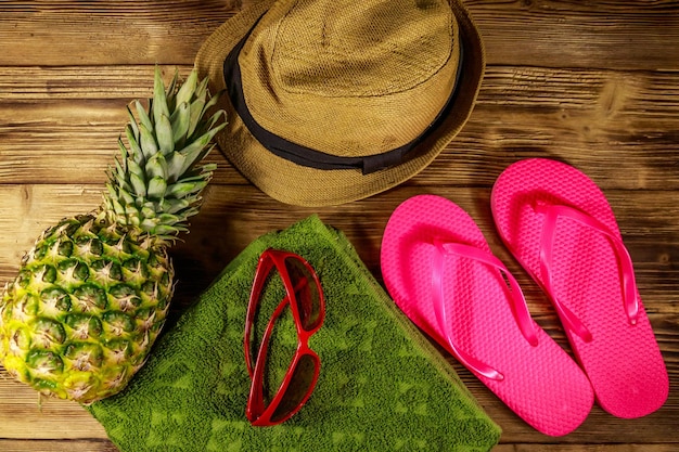 Sommerferienkonzept Ananas Strohhut Flip Flops Handtuch und Sonnenbrille auf Holzhintergrund