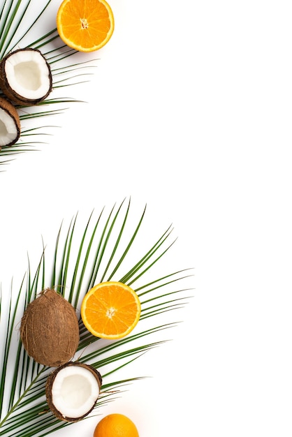 Sommerferienkonzept Vertikales Foto von reifen tropischen Früchten, rissigen Kokosnüssen, orangefarbenen Hälften und grünen Palmblättern auf isoliertem weißem Hintergrund mit leerem Raum