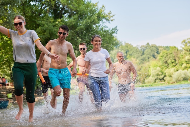 Sommerfreudengruppe fröhlicher Freunde, die sich beim Laufen und Planschen am Fluss amüsieren