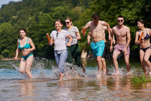 Sommerfreudengruppe fröhlicher Freunde, die sich beim Laufen und Planschen am Fluss amüsieren