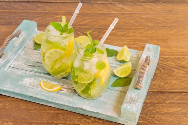 Sommerfrische kalte Limonade mit Limette, Zitrone, Minze und Eis serviert auf blauem Holztablett. Alkoholfreies Getränk.