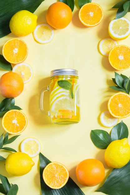 Sommerfrüchte wässern mit Zitrone, Orange, Minze und Eis im Weckglas auf Gelb. Tropisches Konzept.