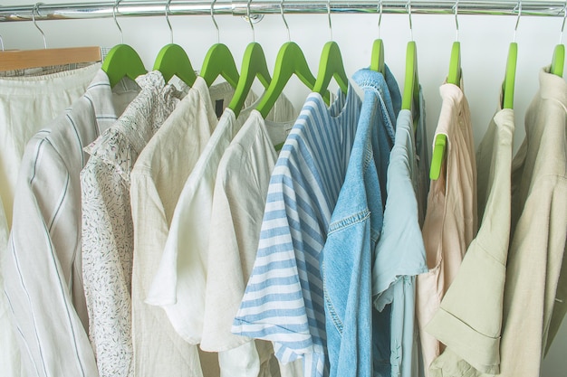 Sommergarderobe mit Leinenkleidung auf grünen Kleiderbügeln