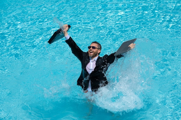 Sommergeschäft im Schwimmbad Geschäftsmann im Anzug und Laptop spritzt Wasser im Schwimmbad verrückt