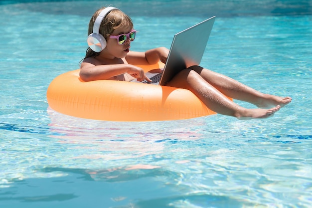 Sommergeschäftskind, das an Laptop-Computer am Swimmingpool am Pool arbeitet Sommer-Online-Technologie tr