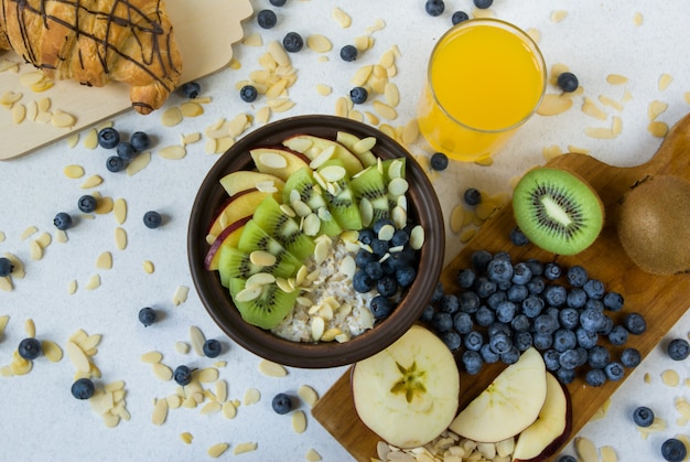 Sommergesundes Frühstück oder Snack. Haferflocken mit Beeren und Früchten, Saft und Krassan auf einem weißen flachen Tisch