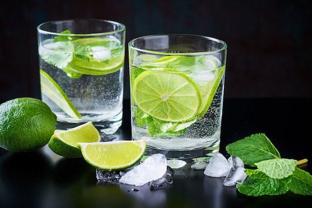 Sommergetränklimonade mojito mit kalk, minze und eis auf einem schwarzen hintergrund