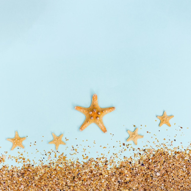 Sommerhintergrund mit gelbem Seestern und Sand auf pastellblauem Konzept von Reisen und Urlaub