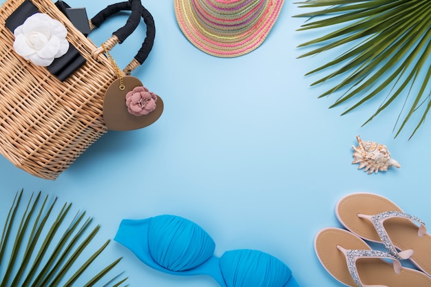 Sommerhintergrund mit Palmblättern, Modehut, Bikini, Flip-Flops, Stroh-Strandtasche auf hellem pastellblauem Hintergrund, Reise- und Urlaubskonzept, Draufsicht