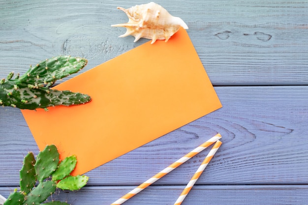 Foto sommerhintergrund orangefarbener umschlag, sukkulenten, cocktailröhren, muschel auf blauem holzhintergrund