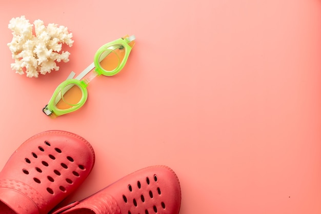 Sommerhintergrund von Crocs, Korallen, Schwimmbrillen, auf rosa Hintergrund