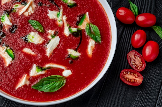 Sommerkalte Tomaten-Gemüsesuppe Gazpacho mit Mozzarella-Käse auf dem schwarzen Tisch Vegetarische Küche