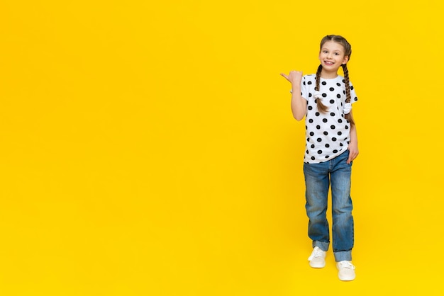 Sommerkleidung auf einem schönen kleinen Mädchen Ein Kind in Jeans und einem gepunkteten T-Shirt auf gelbem Hintergrund