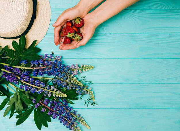 Sommerkonzept, Strohhut, frische Erdbeeren und Blumen auf einem hölzernen Hintergrund