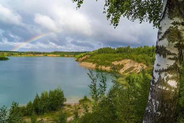 Foto sommerlandschaft mit einem regenbogen in der ferne über wald und wasser