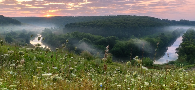 Sommerlandschaft, Morgensonnenschein mit Wolken und Nebel auf dem kleinen Fluss und der Wiese.