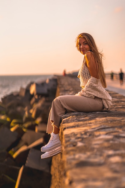 Sommerlebensstil, eine junge blonde kaukasische Frau, die am Meer in einem weißen Erntedach und in Cordhosen sitzt.