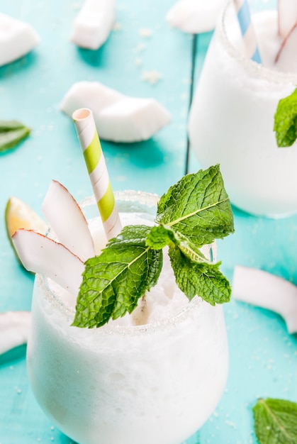 Sommerliche Erfrischungsgetränke, Cocktails. Gefrorener Kokosmojito mit Kalk und Minze. Pina Colada. Auf einem hellblauen grünen Holztisch mit Bestandteilen. Textfreiraum nahaufnahme