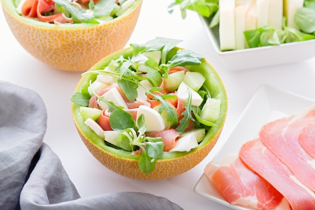 Sommerlicher mediterraner Salat mit Schinken und Melone auf weißer Tischplatte