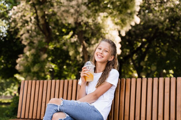 Sommerlimonadencocktail im Freien Glückliches Mädchen, das eine Tasse mit Orangenlimonade hält und lächelt und lacht