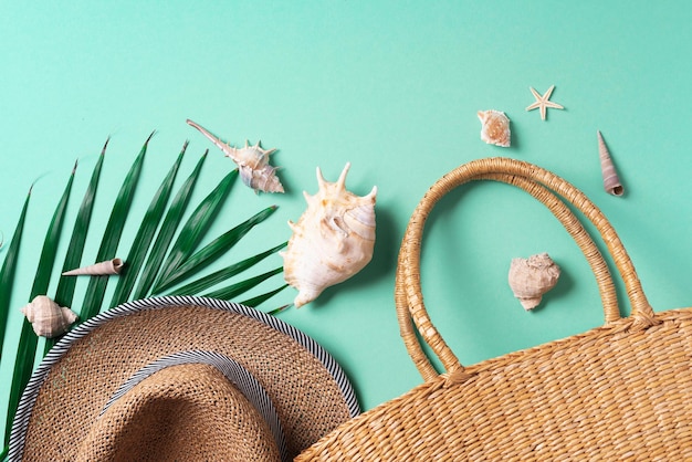 Sommermode flach lag Stilvolle Strohtasche Hut Palmblätter Muscheln auf trendigem grünem Hintergrund Ansicht von oben Kopierbereich Nachhaltiger Lebensstil Konzept ohne Kunststoffabfälle